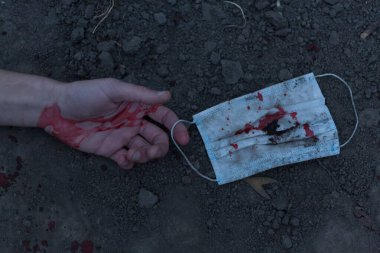Kanlı bir el uzanıp yerde yatan tıbbi kanlı bir maske. Koronavirüs konsepti ve bu hastalığın neden olduğu kıyamet tüm dünyaya yayıldı. Korkunç..