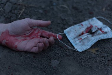 Kanlı bir el uzanıp yerde yatan tıbbi kanlı bir maske. Koronavirüs konsepti ve bu hastalığın neden olduğu kıyamet tüm dünyaya yayıldı. Korkunç..