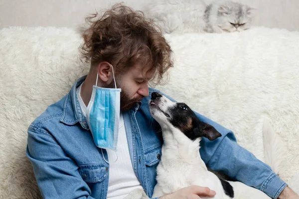 A man with his pet is sitting on a sofa at home. Quarantine coronavirus.