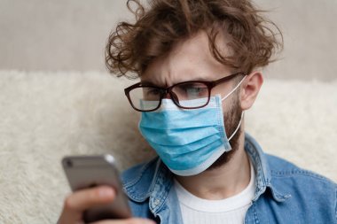 Adam akıllı telefonuyla haberleri seyrediyor. Ev ortamını karantinaya alın. Koronavirüs salgını. Sosyal mesafe. Haberler kötü. Haberler sahte..