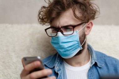 Adam akıllı telefonuyla haberleri seyrediyor. Ev ortamını karantinaya alın. Koronavirüs salgını. Sosyal mesafe. Haberler kötü. Haberler sahte..