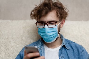 Adam akıllı telefonuyla haberleri seyrediyor. Ev ortamını karantinaya alın. Koronavirüs salgını. Sosyal mesafe. Haberler kötü. Haberler sahte..