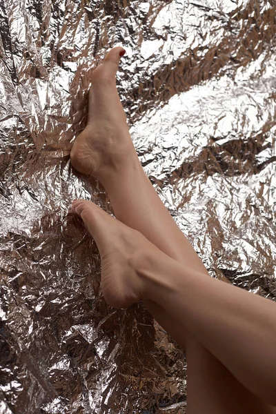 Attractive female legs on a fashionable background in the form of chrome foil. Legs are upper. Red pedicure. Stock photo of beautiful legs.