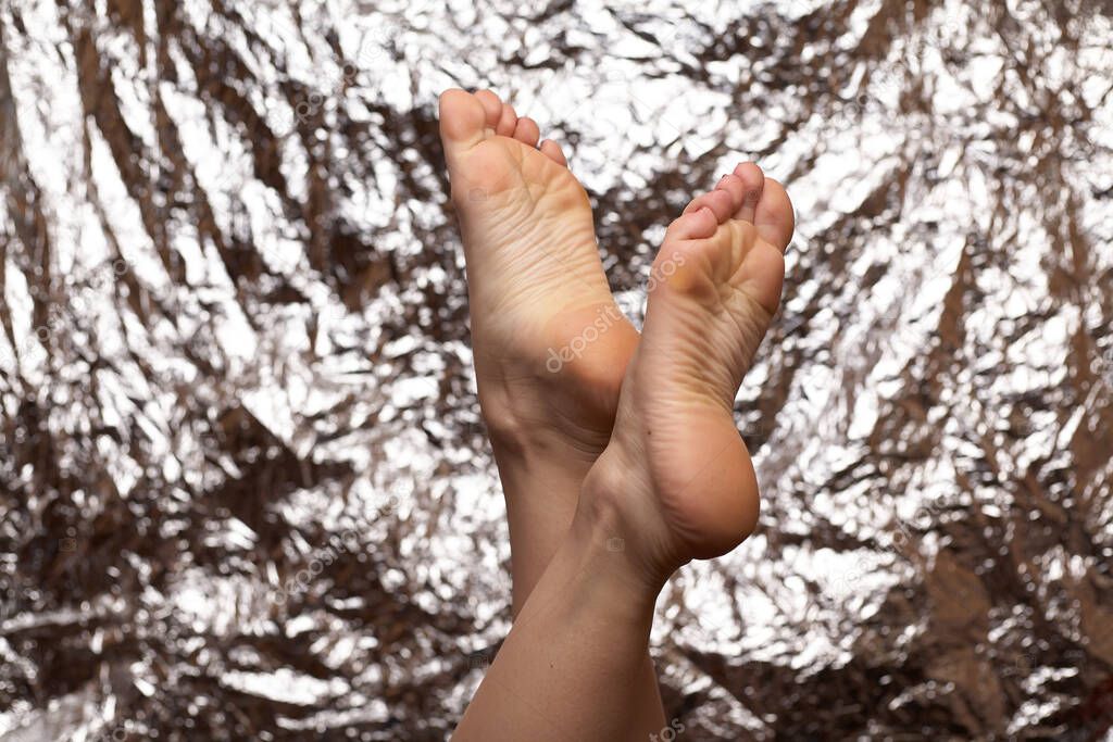 Beautiful female feet on a beautiful background in the form of a foil. Fashionable photo of female legs. Red pedicure.