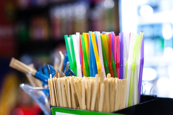 Selective focus on straws on a coffee bar counter with copy space. Plastic Straws, wooden stirrer, and sugar sticks on a blur against a coffee shop background.