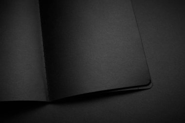 Siyah masadaki boş siyah defter, sahte fotoğraf. Tasarım için kopyalama alanı olan boş siyah kapak şablonu. Siyah üzerine siyah, minimal tasarım konsepti.