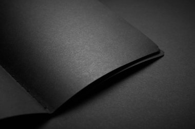 Siyah masadaki boş siyah defter, sahte fotoğraf. Tasarım için kopyalama alanı olan boş siyah kapak şablonu. Siyah üzerine siyah, minimal tasarım konsepti.