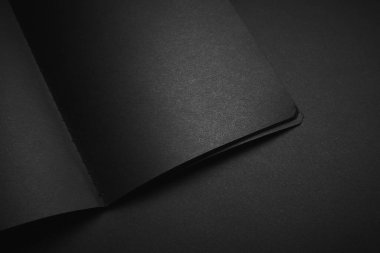 Siyah masadaki boş siyah defter, sahte fotoğraf. Tasarım için kopyalama alanı olan boş siyah kapak şablonu. Siyah üzerine siyah, minimal tasarım konsepti.