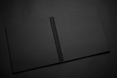 Siyah masadaki boş siyah defter, sahte fotoğraf. Tasarım için kopyalama alanı olan boş siyah kapak şablonu. Siyah üzerine siyah, minimal tasarım konsepti.