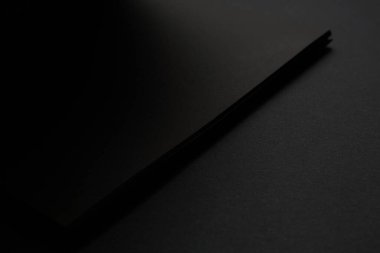 Siyah masadaki boş siyah defter, sahte fotoğraf. Tasarım için kopyalama alanı olan boş siyah kapak şablonu. Siyah üzerine siyah, minimal tasarım konsepti.