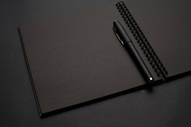 Siyah masadaki boş siyah defter, sahte fotoğraf. Tasarım için kopyalama alanı olan boş siyah kapak şablonu. Siyah üzerine siyah, minimal tasarım konsepti.