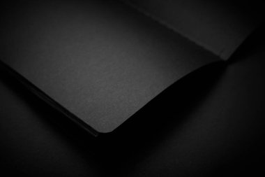 Siyah masadaki boş siyah defter, sahte fotoğraf. Tasarım için kopyalama alanı olan boş siyah kapak şablonu. Siyah üzerine siyah, minimal tasarım konsepti.