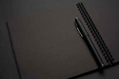 Siyah masadaki boş siyah defter, sahte fotoğraf. Tasarım için kopyalama alanı olan boş siyah kapak şablonu. Siyah üzerine siyah, minimal tasarım konsepti.