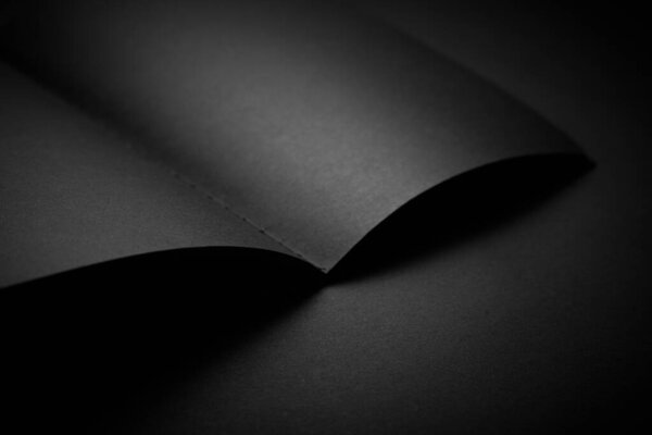 Blank black notebook on a black table, mockup photo. Blank black cover template with copy space for design. Black on black, minimal design concept.