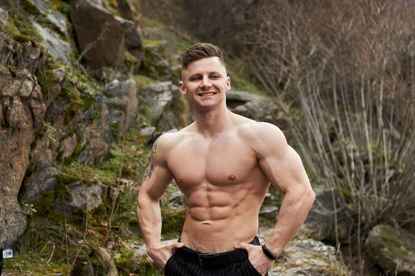 Attractive young guy demonstrates muscular torso outdoors. Beautiful physique. Fitness and lifestyle concept. Pronounced muscles of the press. Athletic physique.