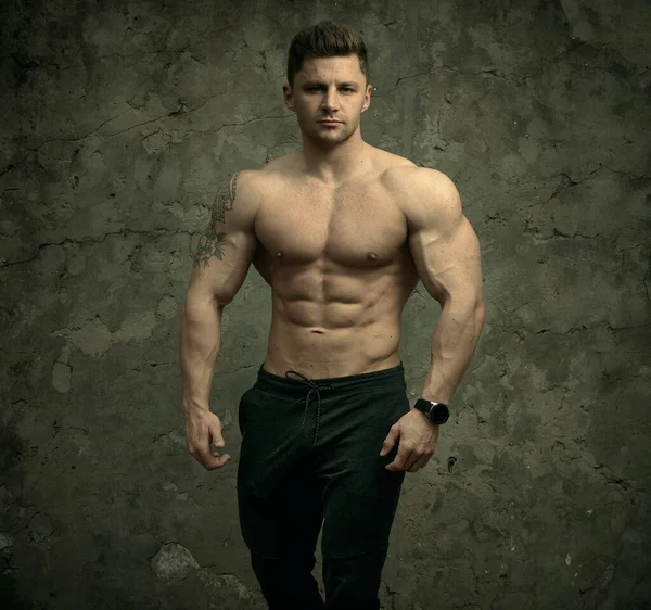 Beton duvarda poz veren yakışıklı kaslı adam. Fitness konsepti, vücut geliştirme, sağlık, yaşam tarzı. Fitness fitness modelinin portresi.