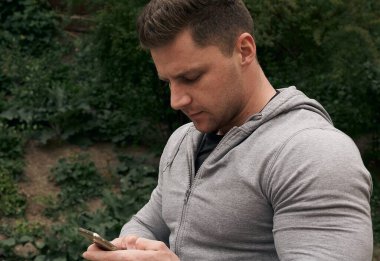 Adam eğitim için akıllı telefon kullanıyor. Atletik adam dışarıda antrenman yapıyor. Eğitim için mobil uygulamayı kavra.