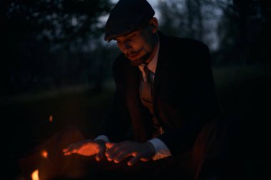 Geceleri şöminenin başında oturan bir adamın portresi. Sinematik klasik fotoğraf. 1920 'lerden kalma düz şapkalı bir İngiliz portresi..