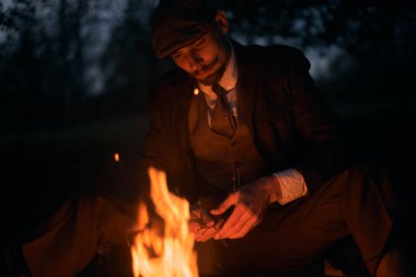 Geceleri şöminenin başında oturan bir adamın portresi. Sinematik klasik fotoğraf. 1920 'lerden kalma düz şapkalı bir İngiliz portresi..