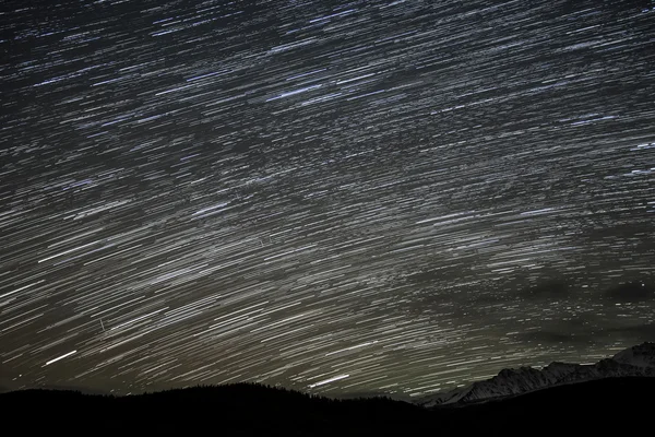 トラックの形で星と山と雪に覆われたピーク 長時間露光で撮影の輪郭を背景に夜の空には雲の痕跡と美しい夜景 — ストック写真