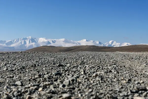 Bir ısmarlayarak bozkır, güneşli bir günde kar ve mavi gökyüzü arka plan tepelerde kaplı dağlar bir çakıl yol ile