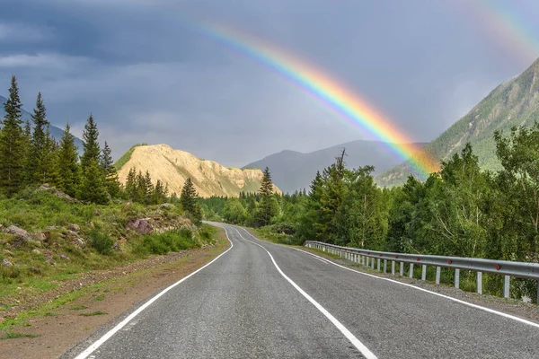 Vägen bergskog rainbow molnigt Stockbild