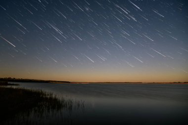 Gece gökyüzünün güzel manzarası. Yıldızlar gölün üzerinde izler, çimenler de ön planda.