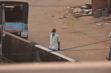Hindistan 'da kilit altında tutulurken polis cipinin yanında yürüyen maske takan biri, covid ya da corona yüzünden..