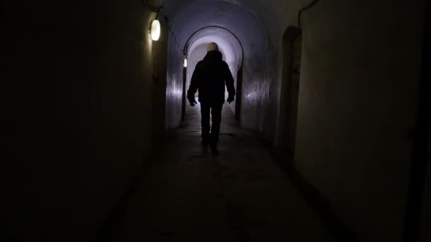 Man in a black jacket walks down a long dark tunnel — Stock Footage Man Black Jacket Walks Long Dark Tunnel Video Clip