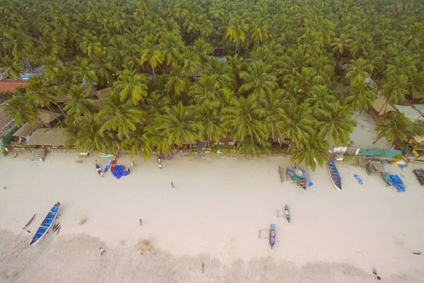 Aerial view of beautiful coastline of Indian ocean with tropical forest, sandy beach, calm blue water and fishing boats in Goa