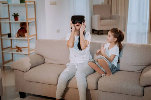 Mãe com o filho ter um bom tempo juntos eles jogando no jogo de vídeo, mãe usando um VR para explorar o mundo virtual, eles sentados no sofá em uma espaçosa sala de estar — Fotografia de Stock