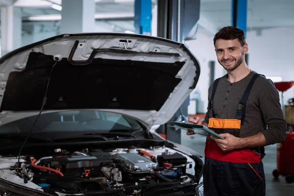 Hombre mecánico en un uniforme sonriendo grande delante de la cámara en un moderno centro de servicio automático — Foto de Stock