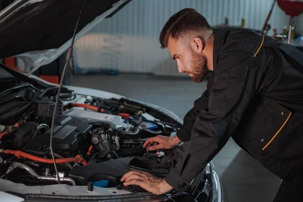 Een jonge monteur is zeer gericht op het kijken naar de motor van de auto die hij moet repareren — Stockfoto