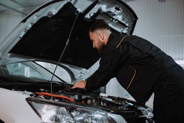 İyi görünümlü tamirci arabanın motoru üzerinde çalışıyor. Problemi kameranın önünde çözüyor. Çok konsantre çalışıyor.