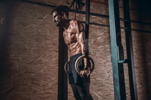 Em uma aula de ginástica escura atlético forte cara começando seu treinamento de trabalho duro, ele equilibrando os anéis de esporte — Fotografia de Stock