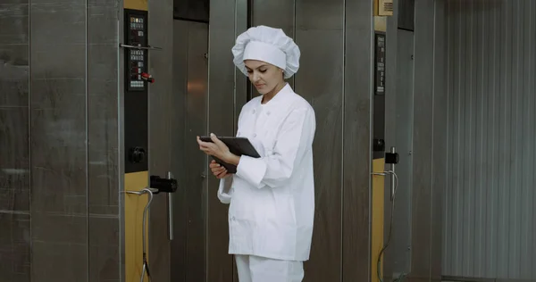 Volwassen vrouw, het controleren van de industriële oven machine neemt enkele notities op de tablet — Stockfoto