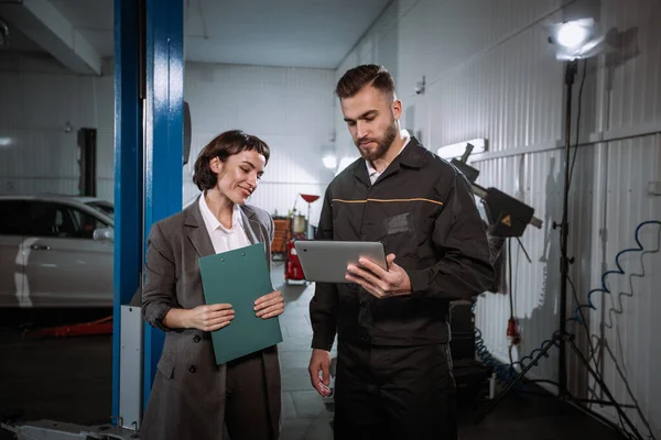 Mechanik centrum serwisowego rozmawia z klientką. Pokazują mu coś na tablecie. — Zdjęcie stockowe