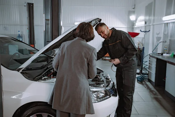 Servicio mecánico de centro automático tener una conversación con la mujer cliente que le muestra algo en el motor del coche — Foto de Stock