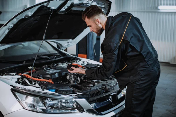 Chico mecánico de buen aspecto en un auto de servicio moderno comprobar cuidadosamente el nivel de aceite del coche —  Fotos de Stock