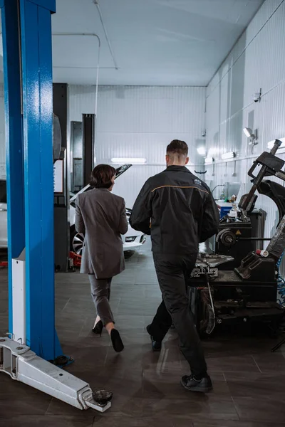 Em um carro serviço de centro de boa aparência mulher em um terno de negócios ela vai para o carro para verificar o problema em uma garagem de automóveis — Fotografia de Stock