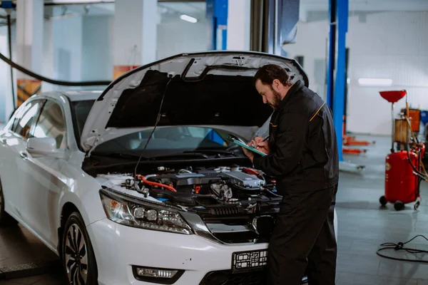 Mechanik w mundurze napisać problem samochodu na mapie w nowoczesnym centrum serwisowym — Zdjęcie stockowe