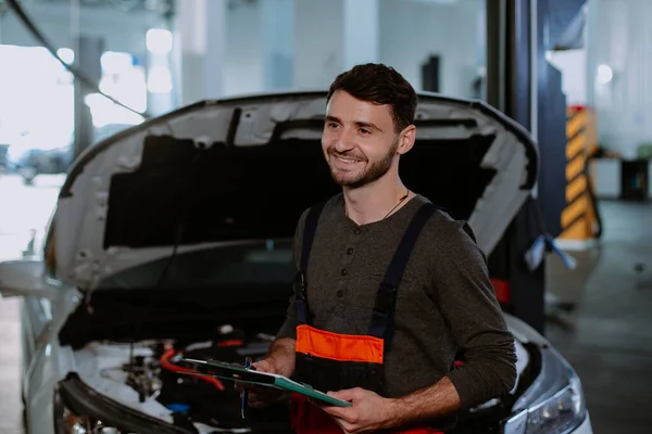 Mechanik w mundurze uśmiechnięty duży przed kamerą w nowoczesnym centrum serwisu samochodowego — Zdjęcie stockowe