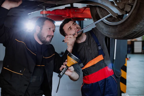 Twee grappige arbeiders analyseren de auto eronder, die beide zeer geconcentreerd zijn. — Stockfoto