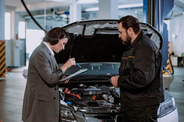 De manager van een auto service center hebben een gesprek met de volwassen monteur man ze analyseren van het probleem van de auto te schrijven op de kaart — Stockfoto