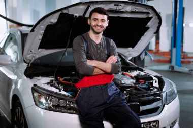 Modern bir oto hizmet merkezinde kameranın önünde gülümseyen üniformalı tamirci.