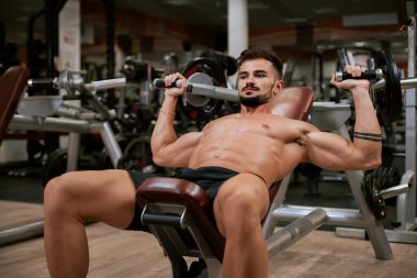 Spor salonunda barbell tezgah basın egzersiz yapıyor Gömleksiz kaslı genç adam