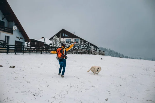 Szczęśliwy i charyzmatyczny facet przybył do miejsca przeznaczenia on i ciesząc się krajobrazem przyrody i śnieżnej góry bawiąc się z psem — Zdjęcie stockowe