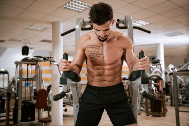 Spor salonunda barbell tezgah basın egzersiz yapıyor Gömleksiz kaslı genç adam
