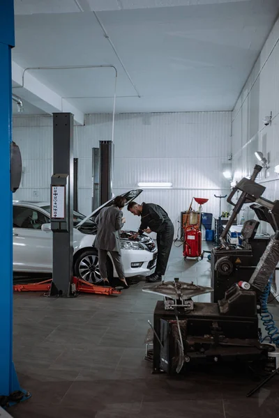 Em um carro serviço de centro de boa aparência mulher em um terno de negócios ela vai para o carro para verificar o problema em uma garagem de automóveis — Fotografia de Stock