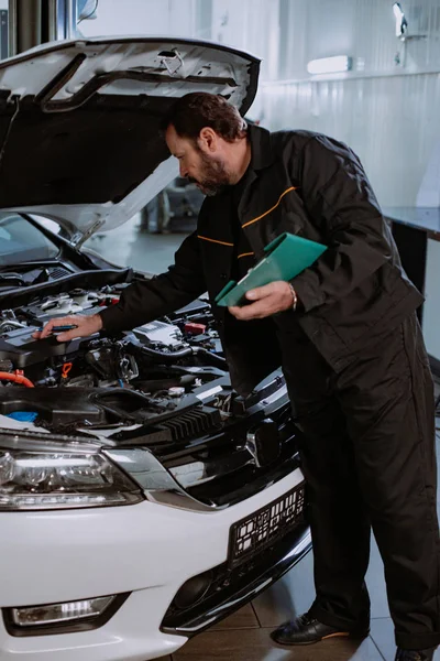 Hombre mecánico en uniforme escribir el problema del coche en un mapa en el moderno centro de servicio — Foto de Stock